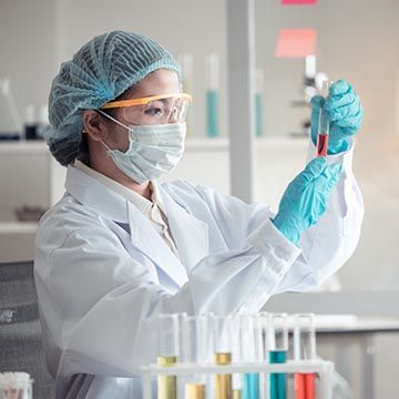 A scientist wearing a mask and laboratory attire, and holding a test tube